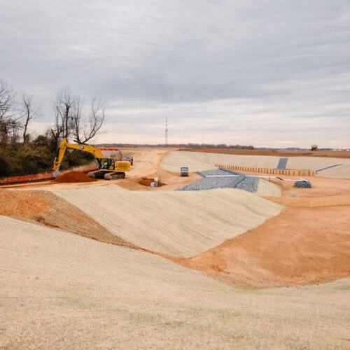 Excavator and dirt mounds on a cloudy construction site.