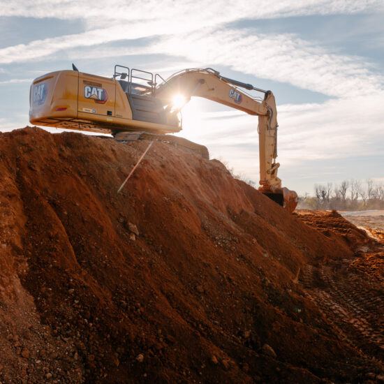 Yellow Caterpillar excavator on dirt mound at construction site.