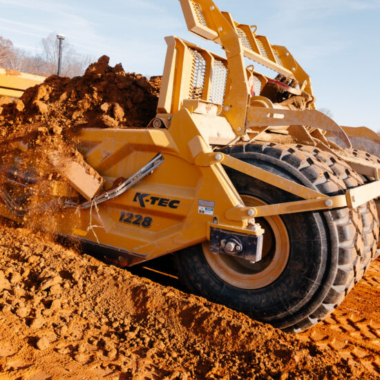 Yellow K-Tec 1228 earthmover levels reddish-brown soil.