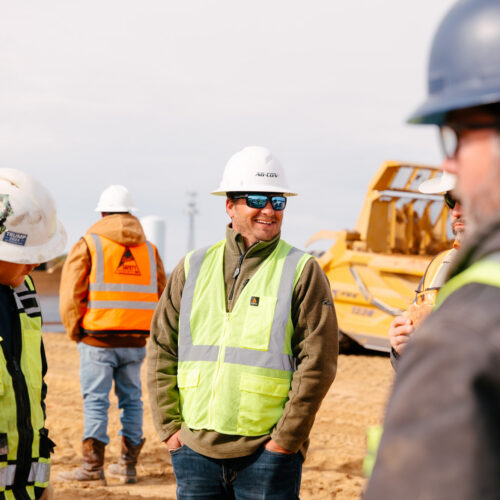 Construction workers in vests and hard hats talk at site.