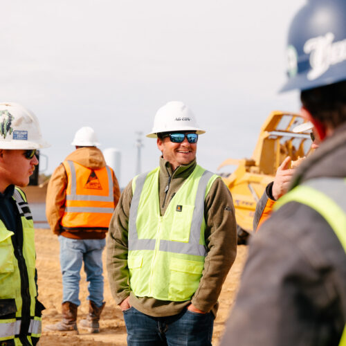 Four construction workers talk at a site with machinery.