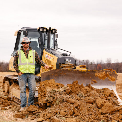 Person in hard hat by yellow bulldozer at construction site.