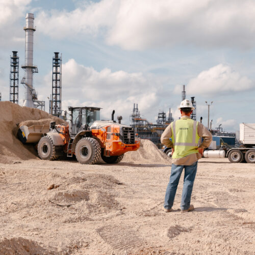 Worker in safety vest watches front loader move sand on site.