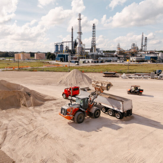Front loader fills dump truck at industrial site with silos.