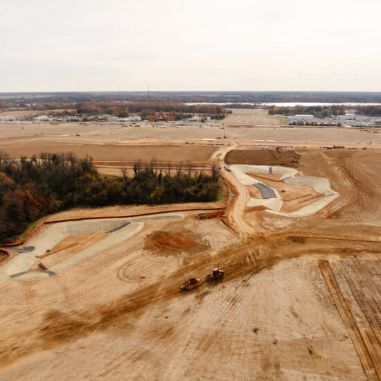 Aerial view of construction site with machinery, dirt roads, trees.